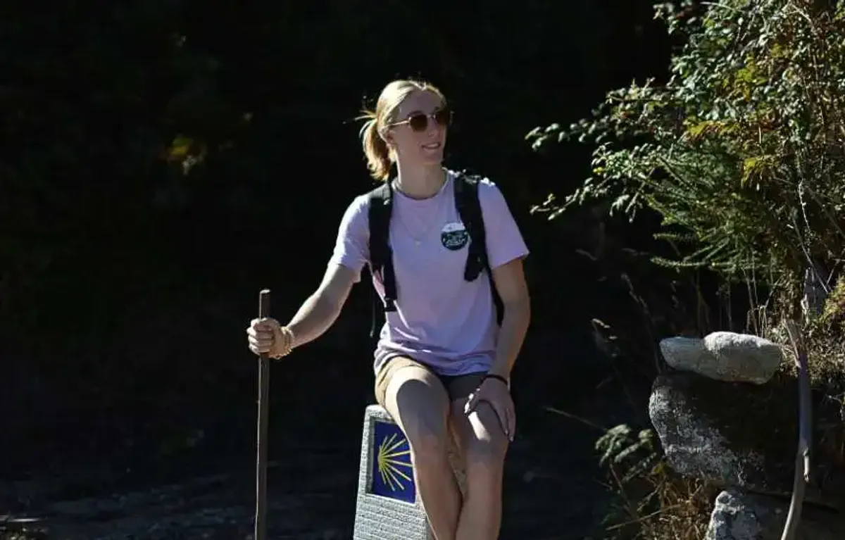 Peregrina sentada sobre mojón del Camino de Santiago