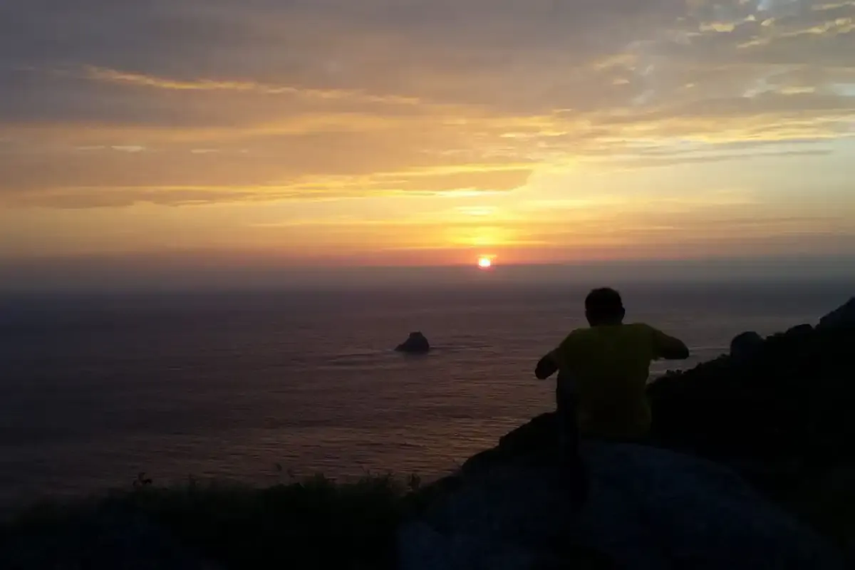 Pèlerin méditant au cap Finisterre en regardant le coucher de soleil