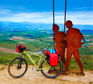 Una bici con alforjas apoyada en el monumento del Alto del Perdón