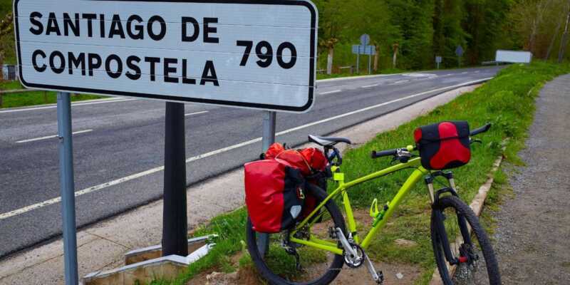 Una bicicleta con alforjas apoyada en un cartel a Santiago