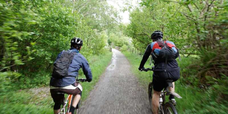 Dos personas montando en bici por un sendero boscoso