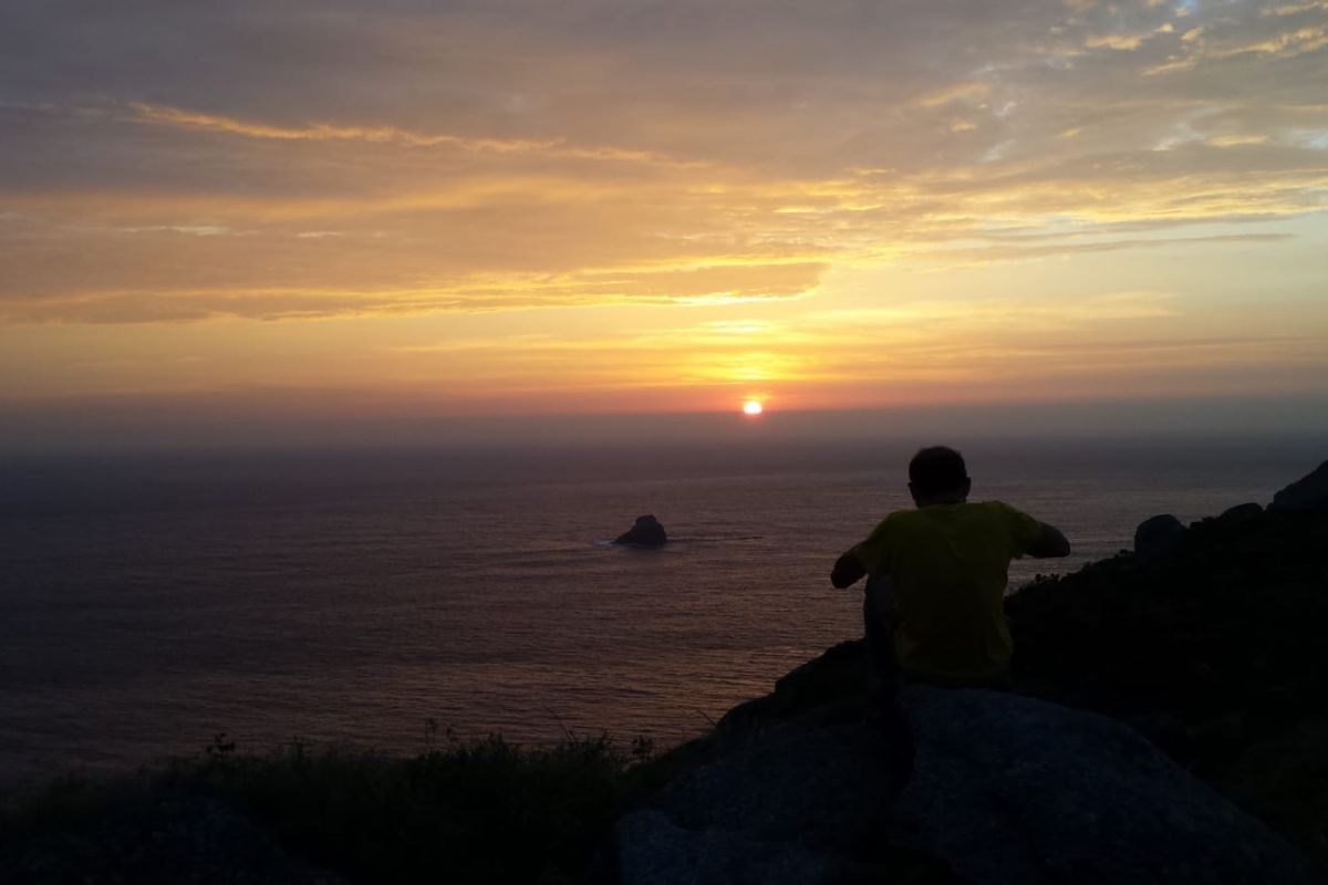 Peregrino reflexionando en el cabo Finisterre, viendo la puesta de sol.